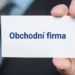 Ruka v obleku drží vizitku s nápisem "Obchodní firma", symbolizující ochranu názvu společnosti.
